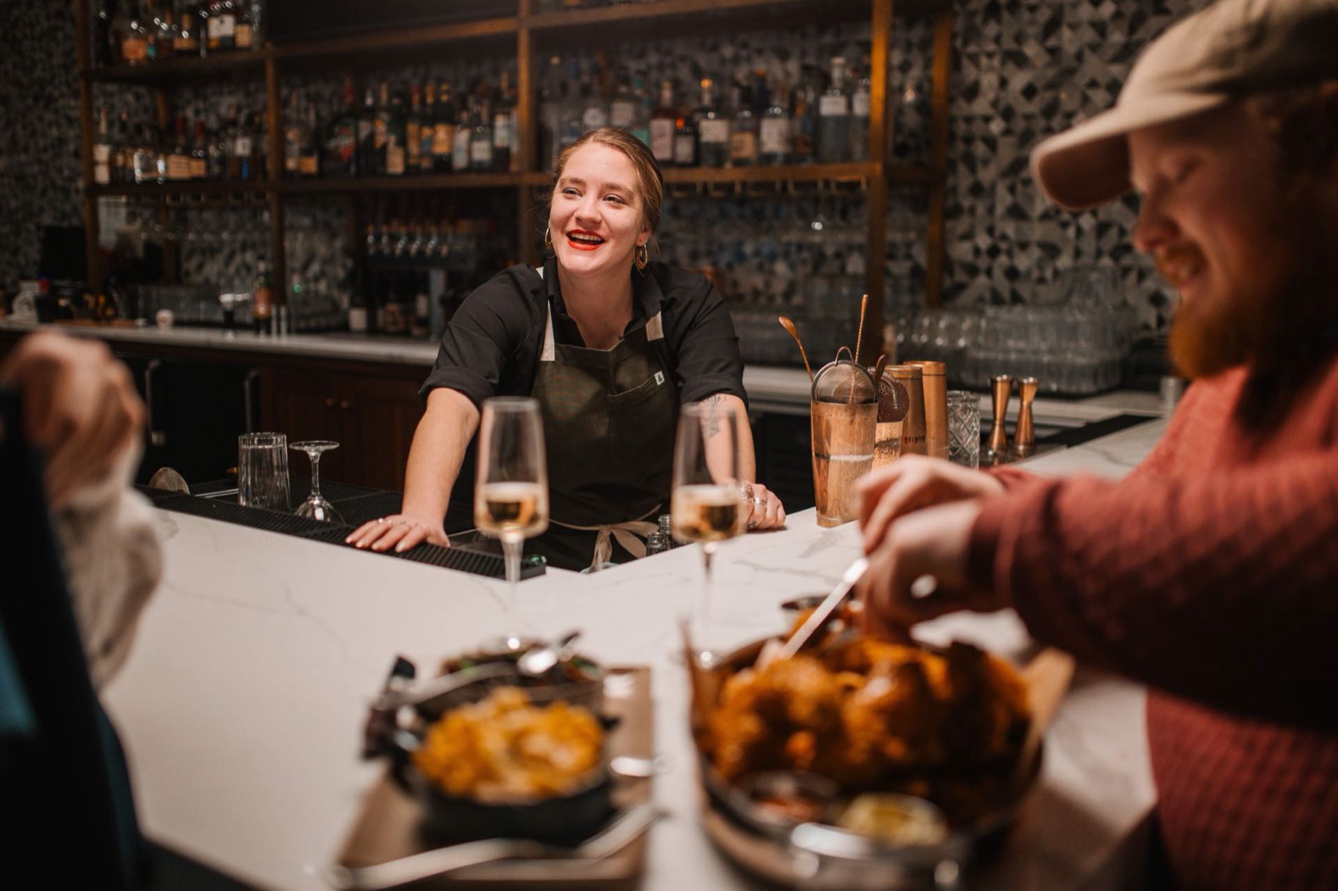 A GHG bartender laughing with two guests across the bar